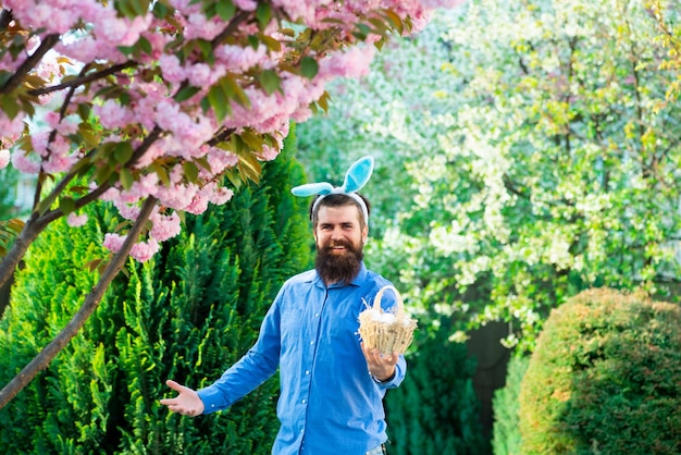 Fröhlicher ostermann vorbereitung auf ostern glücklicher bärtiger mann mit hasenohren hält korb mit eiern draußen