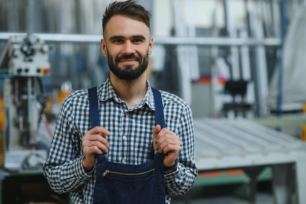 Fröhlicher professioneller Schwerindustrie-Ingenieur, der Uniform und Schutzhelm in einer Stahlfabrik trägt Lächelnder Industriespezialist, der in einer Metallbau-Fertigung steht