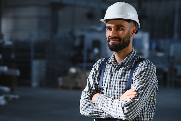 Fröhlicher professioneller Schwerindustrie-Ingenieur, der Uniform und Schutzhelm in einer Stahlfabrik trägt Lächelnder Industriespezialist, der in einer Metallbau-Fertigung steht