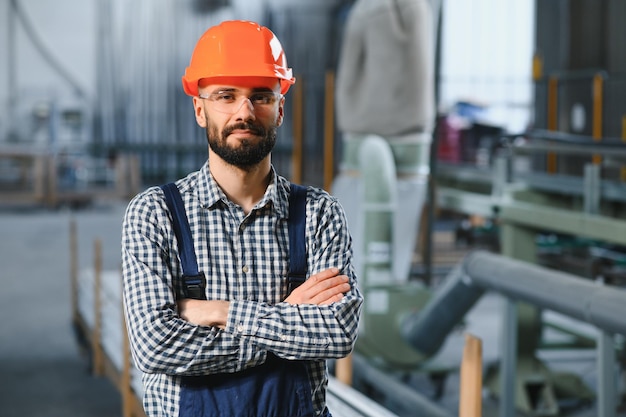 Foto fröhlicher professioneller schwerindustrie-ingenieur, der uniform und schutzhelm in einer stahlfabrik trägt lächelnder industriespezialist, der in einer metallbau-fertigung steht