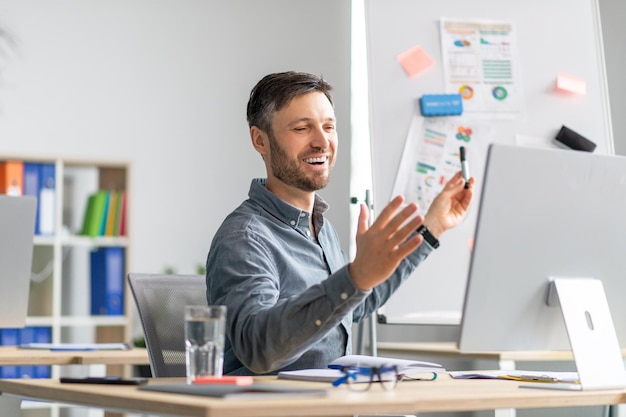 Foto fröhlicher reifer mann, der im büro am computer spricht und grafiken und diagramme demonstriert