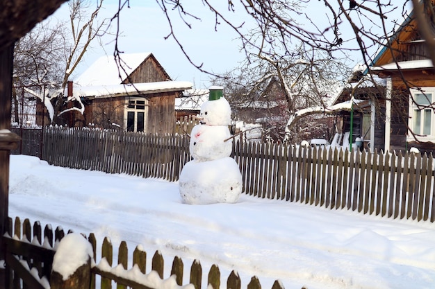 Fröhlicher Schneemann im Hof eines Dorfhauses an einem Wintertag im Januar, Seitenansicht