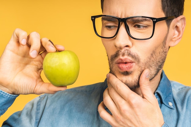 Foto fröhlicher schöner mann, der apfel isoliert über gelbem hintergrund isst