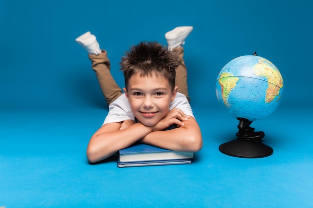 Fröhlicher Schüler sitzt auf blauem Hintergrund mit einem Rucksack und einem Globus-Bildungskonzept