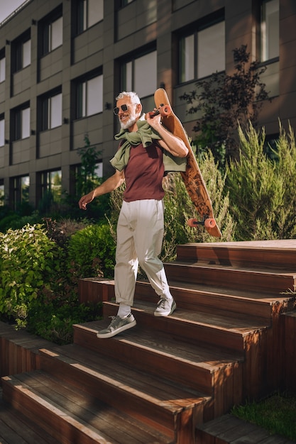 Fröhlicher Skateboardfahrer mit Sonnenbrille, der die Holztreppe hinuntergeht