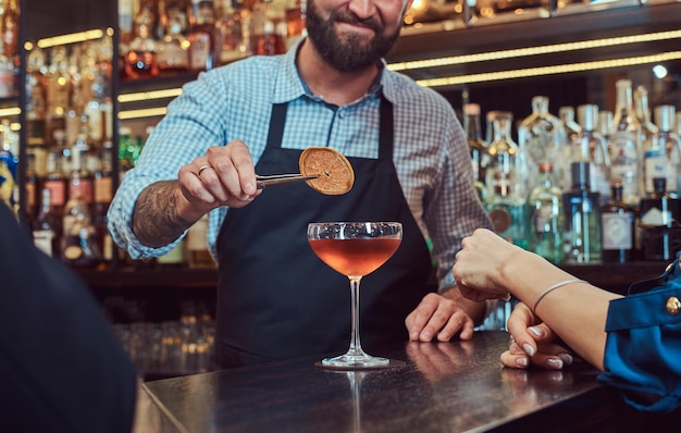 Fröhlicher, stilvoller, brutaler Barkeeper bedient ein attraktives Paar, das einen Abend mit einem Date verbringt.