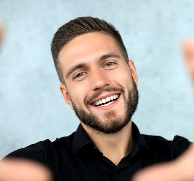 Fröhlicher stilvoller Mann auf grauem Hintergrund macht ein Selfie.
