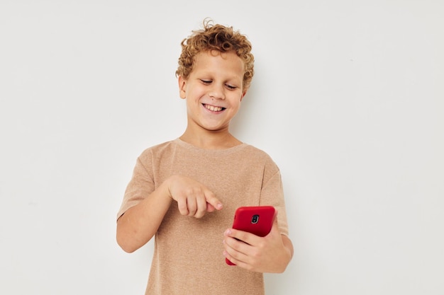 Fröhlicher süßer Junge mit Telefon in Händen, der Technologie aufwirft