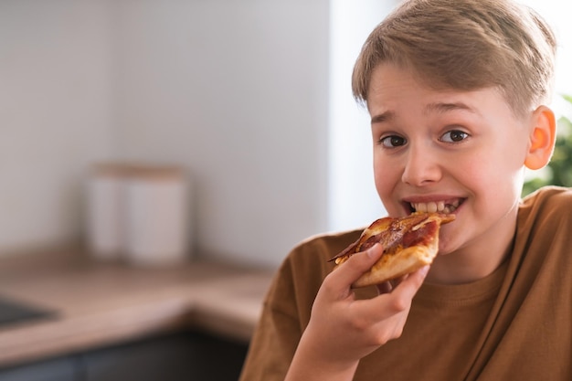 Fröhlicher Teenager, der zu Hause leckere Pizza isst Frisch gebackene Peperoni-Pizza