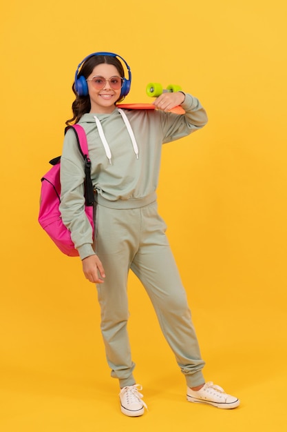 Fröhlicher Teenager in Activewear mit gelbem Pennyboard-Hintergrund, Board-Skating.