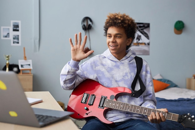 Fröhlicher Teenager in Freizeitkleidung begrüßt seinen Musiklehrer mit einer Handbewegung