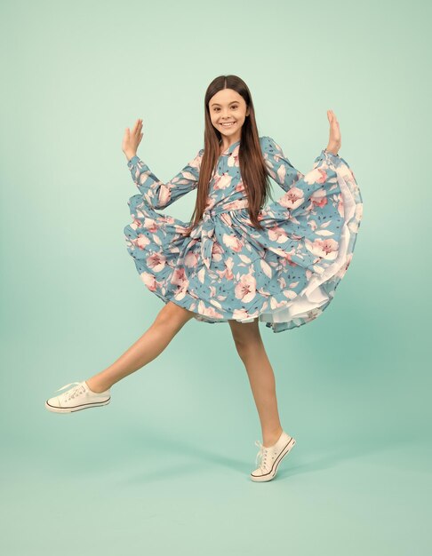 Fröhlicher Teenager-Kindsprung in voller Länge genießen, sich freuen, gewinnen, isoliert auf blauem Hintergrund Kleines Kind Mädchen im Sommerkleid springen