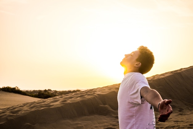 Fröhlicher Teenager mit offenen Armen bei Sonnenuntergang mit Blick auf den Himmel am Strand - nach Monaten der Quarantäne und der Sperrung finnaly free man - Freiheit und Urlaubskonzept und Lebensstil