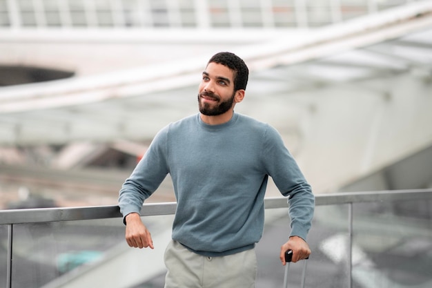 Fröhlicher Tourist aus dem Nahen Osten posiert im Flughafen und schaut zur Seite