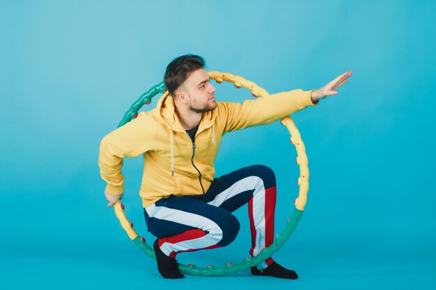Fröhlicher Typ in gelber Bluse mit Hula-Hoop zeigt Gefallen an blauem Hintergrund