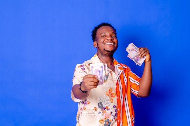 Fröhlicher und aufgeregter junger afrikanischer Mann mit Geldbündeln