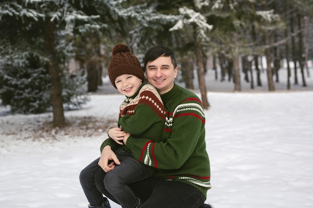 Fröhlicher Vater und Sohn amüsieren sich im Winterwald in Strickpullovern und Mützen