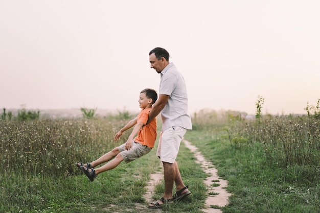 Fröhlicher Vatertag Vater mit Sohn gehen auf dem Feld Papa umarmt Jungen Das Konzept der Vatertagsbeziehungen mit der Fürsorge und Liebe der Kinder