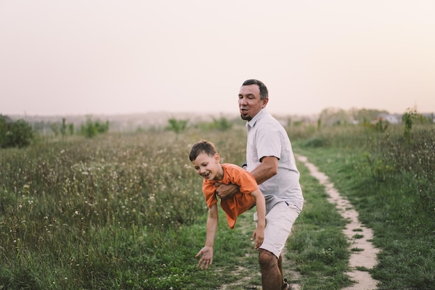 Fröhlicher Vatertag Vater mit Sohn gehen auf dem Feld Papa umarmt Jungen Das Konzept der Vatertagsbeziehungen mit der Fürsorge und Liebe der Kinder