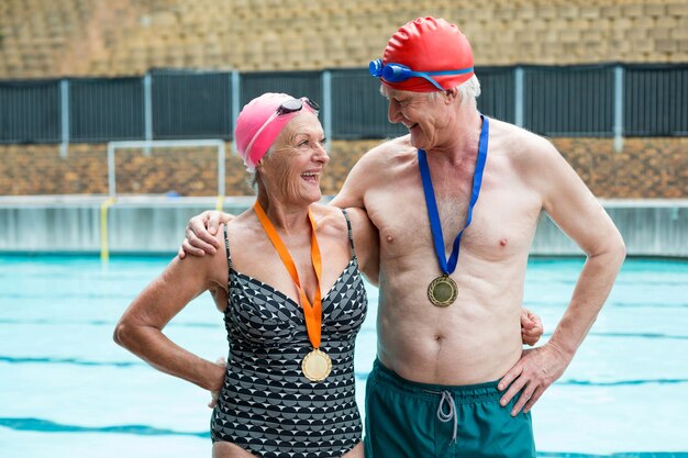 Fröhliches älteres Paar, das Medaillen trägt, während es am Pool steht