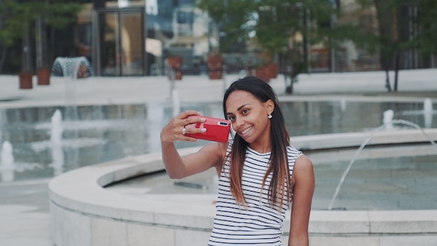 Fröhliches afrikanisches Mädchen, das Selfie vor Brunnen nimmt