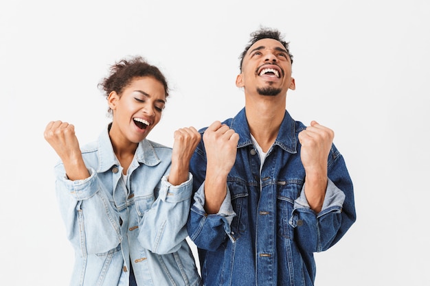 Fröhliches afrikanisches Paar in Jeanshemden freut sich und schreit zusammen über graue Wand