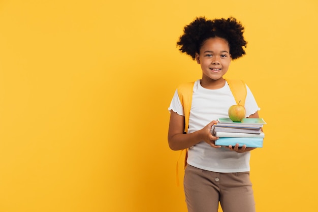 Fröhliches afroamerikanisches Schulmädchen, das Notizbücher und Bücher auf gelbem Hintergrund hält, kopieren Platz