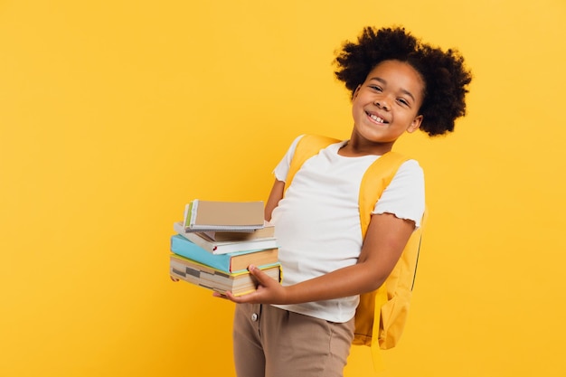 Fröhliches afroamerikanisches Schulmädchen, das Notizbücher und Bücher auf gelbem Hintergrund hält, kopieren Platz