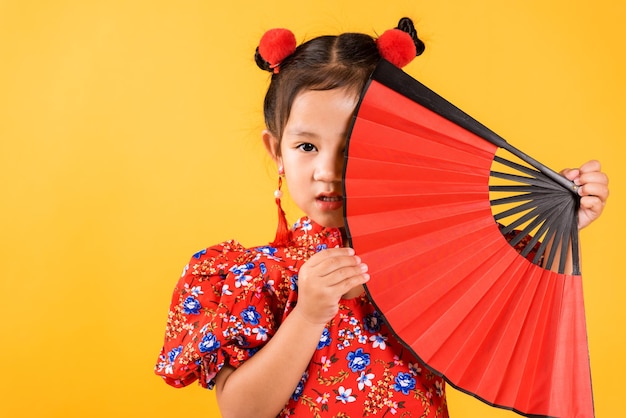 Fröhliches asiatisches chinesisches kleines Mädchen lächelt mit rotem Cheongsam, das einen Fan hält