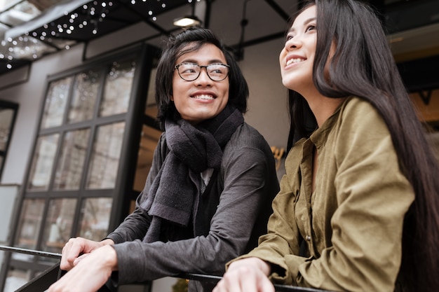 Fröhliches asiatisches junges liebendes Paar, das nahe Café draußen steht