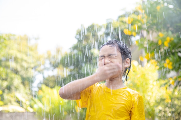 Fröhliches asiatisches kleines Kindermädchen, das Spaß hat, mit dem Regen im Sonnenlicht zu spielen