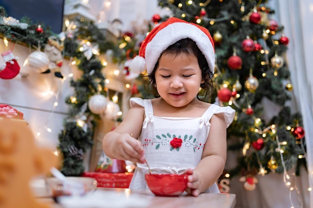 Fröhliches asiatisches kleines Mädchen, das zu Hause mit den Eltern für den Weihnachtstag Lebkuchen kocht. Hausgemachte Weihnachtsplätzchen für Kinder.