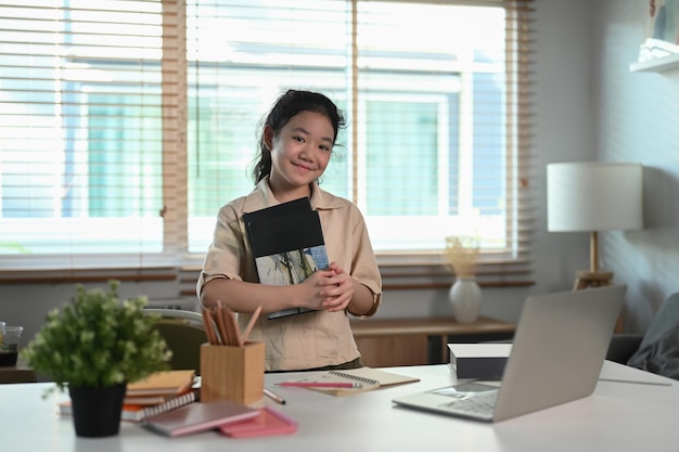 Fröhliches asiatisches Mädchen, das Buch hält und in die Kamera lächelt