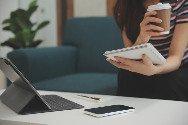 Fröhliches asiatisches Teenager-Mädchen hält ein Pad-Computergerät mit digitaler Tablet-Technologie in der Hand und sitzt zu Hause auf der Couch. Lächelnde junge Frau, die Apps nutzt, um online einzukaufen, Nachrichten zu lesen und auf dem Sofa im Internet zu surfen