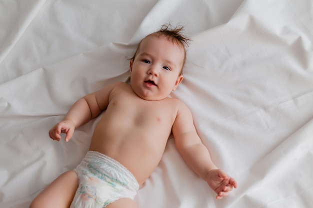 Fröhliches Baby in einer Windel liegt auf dem Rücken im Bett auf einem weißen Blatt Draufsicht