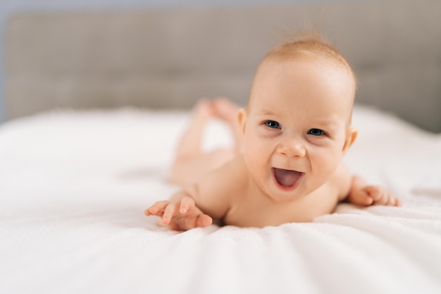 Fröhliches Baby liegt auf dem Schlafzimmerbett und genießt die morgendliche Entspannung zu Hause.