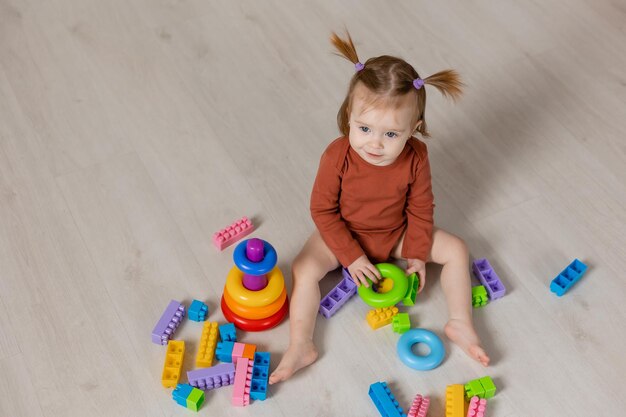 Fröhliches Baby spielt mit einer bunten Pyramide und anderen Lernspielzeugen, die auf dem Boden sitzen