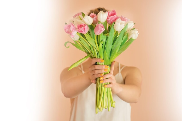 Fröhliches blondes Mädchen, das Tulpenblumenstrauß über beigem Hintergrund hält Porträt eines glücklichen jungen Mädchens in Freizeitkleidung, das einen Tulpenblumenstrauß nimmt