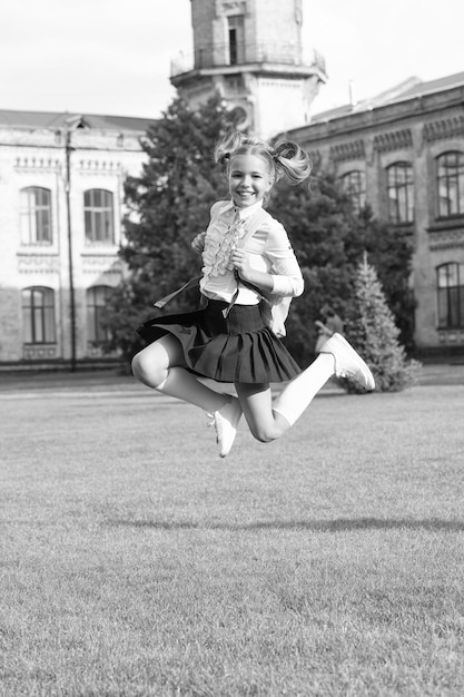 Fröhliches, energisches Kind in Uniform, das am 1. September vor Freude in die Schule springt