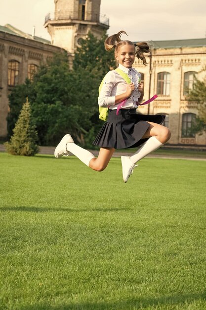 Fröhliches, energisches Mädchen in Uniform zurück zur Schule, das am 1. September vor Freude springt