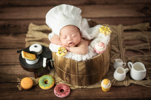Fröhliches entzückendes süßes asiatisches Neugeborenes mit Kochmütze, das mit Donuts-Stütze schläft