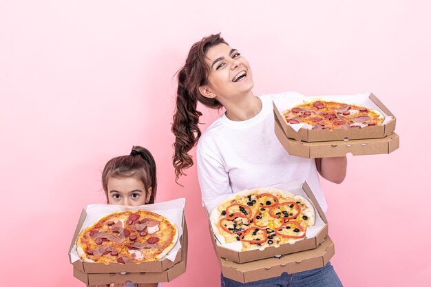 Fröhliches erwachsenes Mädchen und ihre kleine Schwester mit Pizza in Kartons zur Lieferung auf rosa Hintergrund.