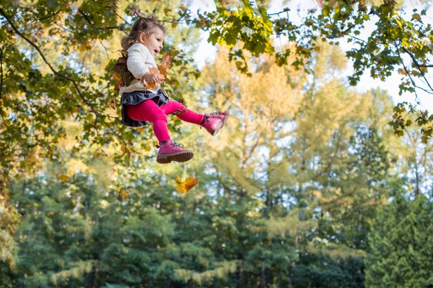 Fröhliches fliegendes springendes Kind im Wald mit Herbstlaub-Emotionsfreude auf dem Gesicht eines Kindes