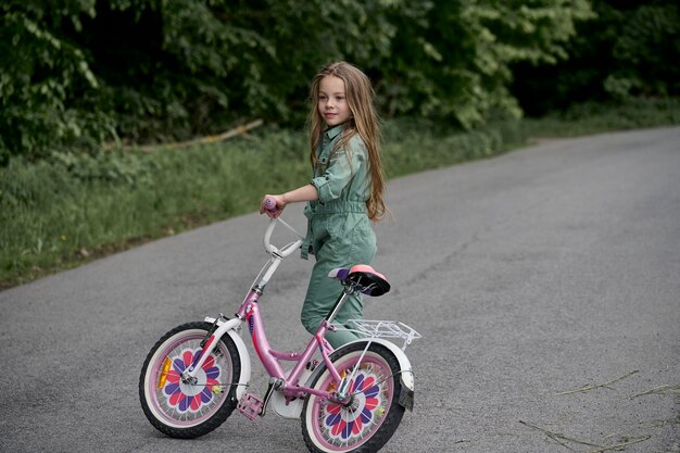 Foto fröhliches, fröhliches kindermädchen, das im park in der natur fahrrad fährt