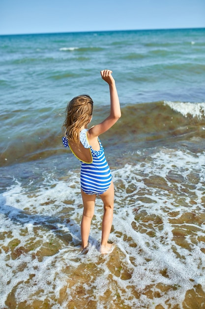 Fröhliches, fröhliches kleines Mädchen, das am Strand läuft