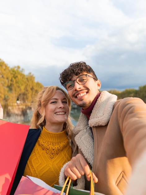 Fröhliches gemischtrassiges Paar von Freunden, die ein Selfie in der Stadt machen und Einkaufstüten in den Händen halten