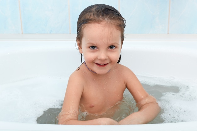 Fröhliches glückliches Kleinkindbaby, das Bad nimmt. Kleines Kind in der Badewanne, entspannend in warmem Wasser.