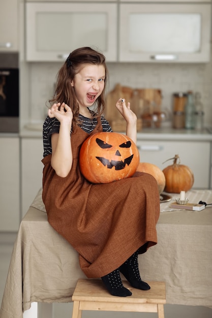Fröhliches Halloween. Nettes kleines Mädchen im Hexenkostüm mit schnitzendem Kürbis. Glückliche Familie, die sich auf Halloween vorbereitet.