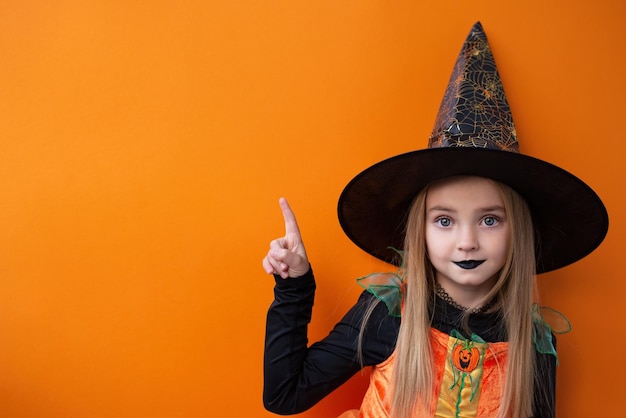 Fröhliches Halloween! Süße kleine Hexe zeigt mit dem Finger auf den Kopierraum