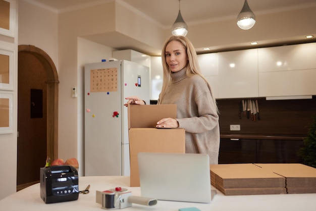 Fröhliches Hausbesitzer-Mietermädchen, das einen Laptop am Stapel gestapelter Kisten verwendet, um die Lieferung zu bestellen